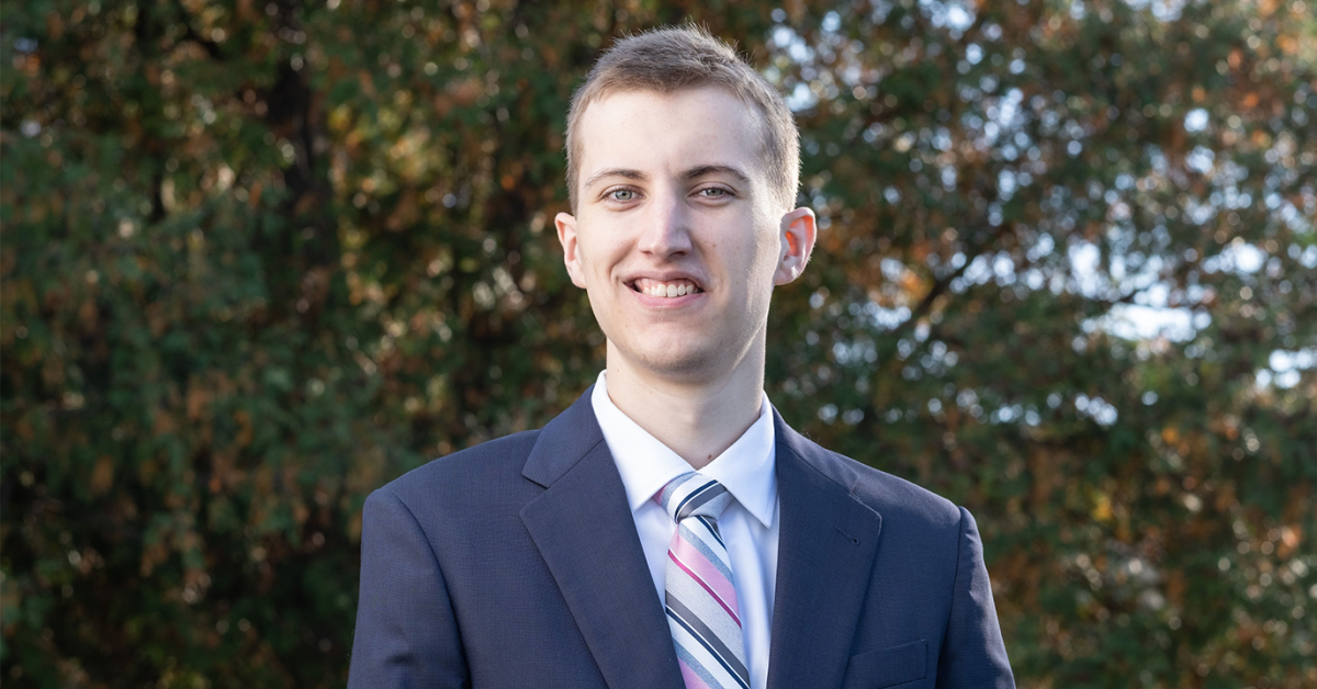John O'Malley stands in front of a leafy green background wearing a suit.