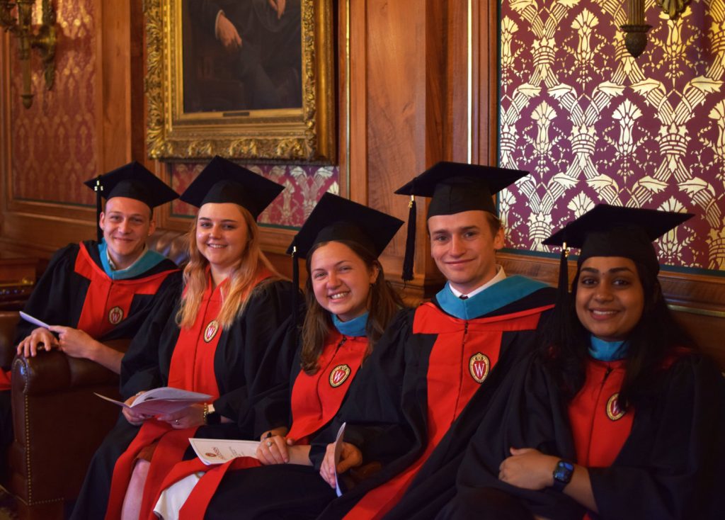 Five students wearing mortarboards and gowns are seated.