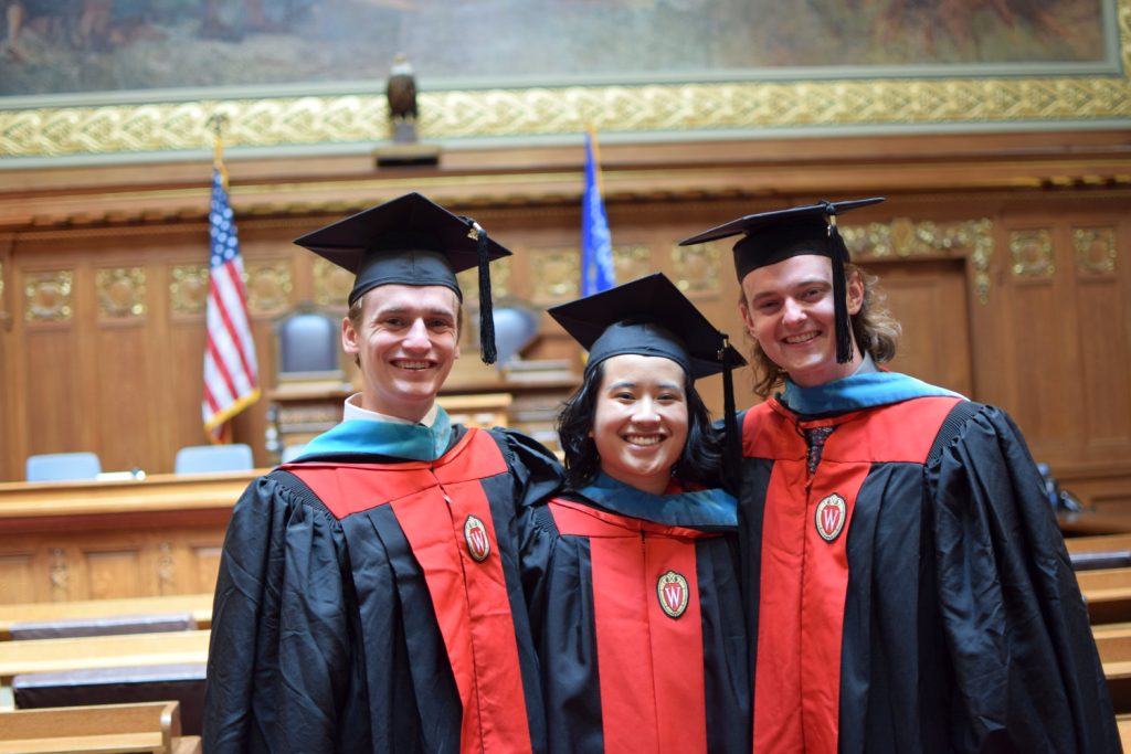 Three students wearing mortarboards and gowns pose for a picture