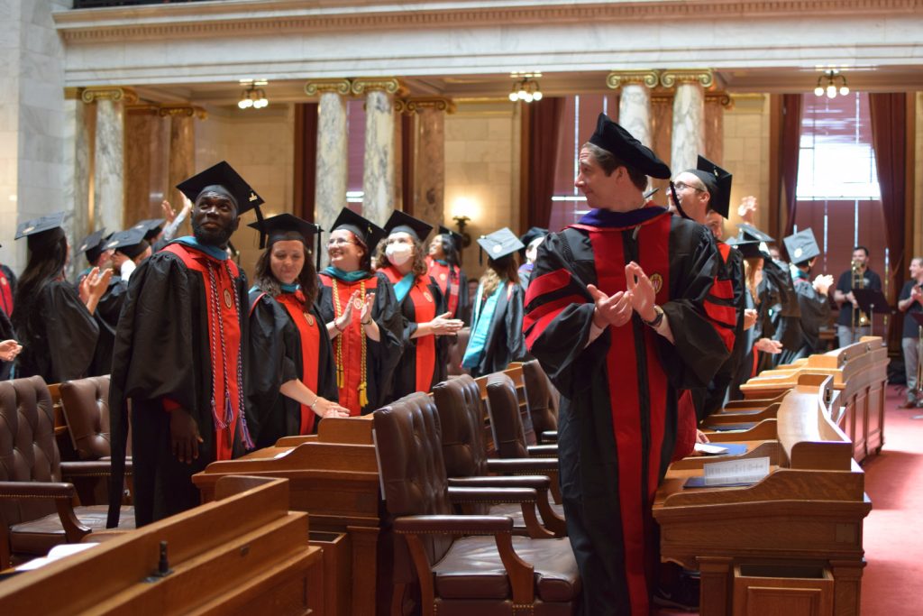 Graduates stand up from their seats in the chambers and clap