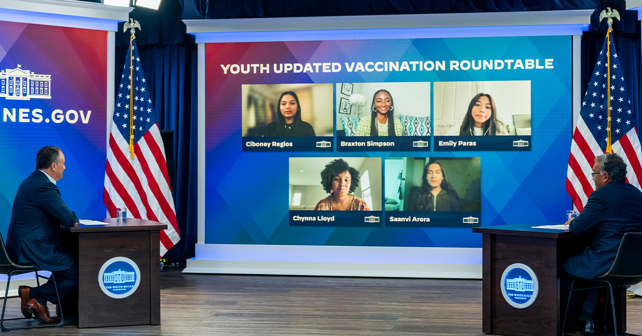 Two staff in suits face a screen displaying a panel of students.