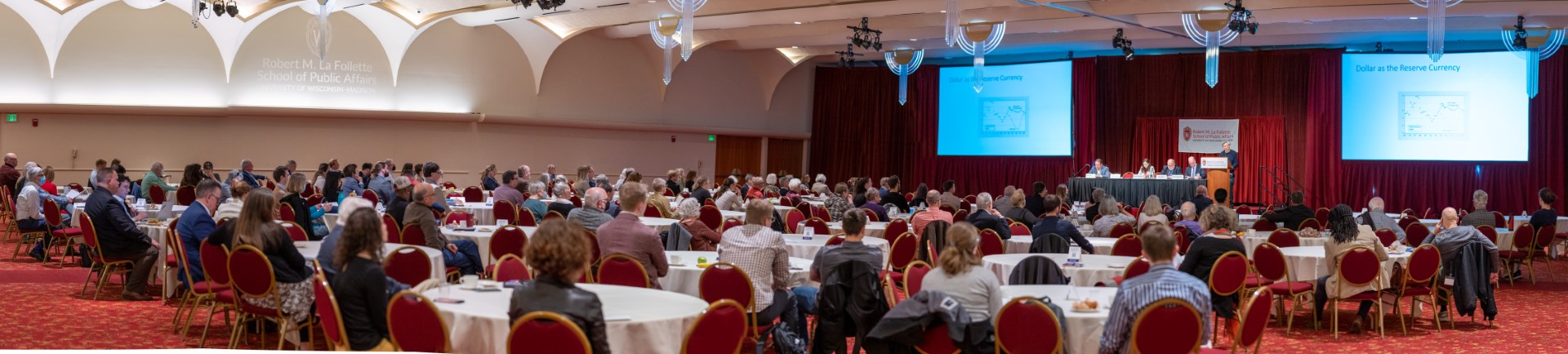 Attendees sit at tables in watching a panel discussion in the Monona Terrace.