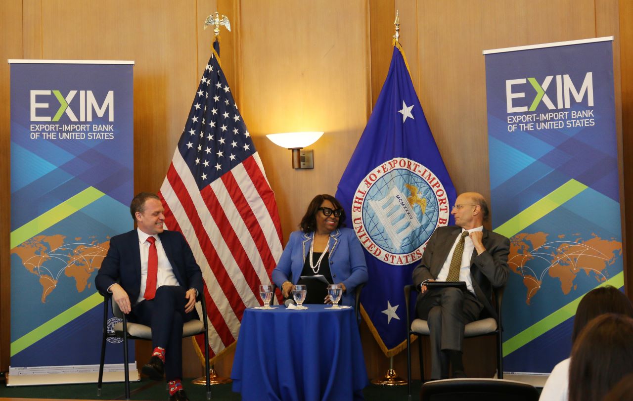 EXIM Bank leaders converse at the front of a room.