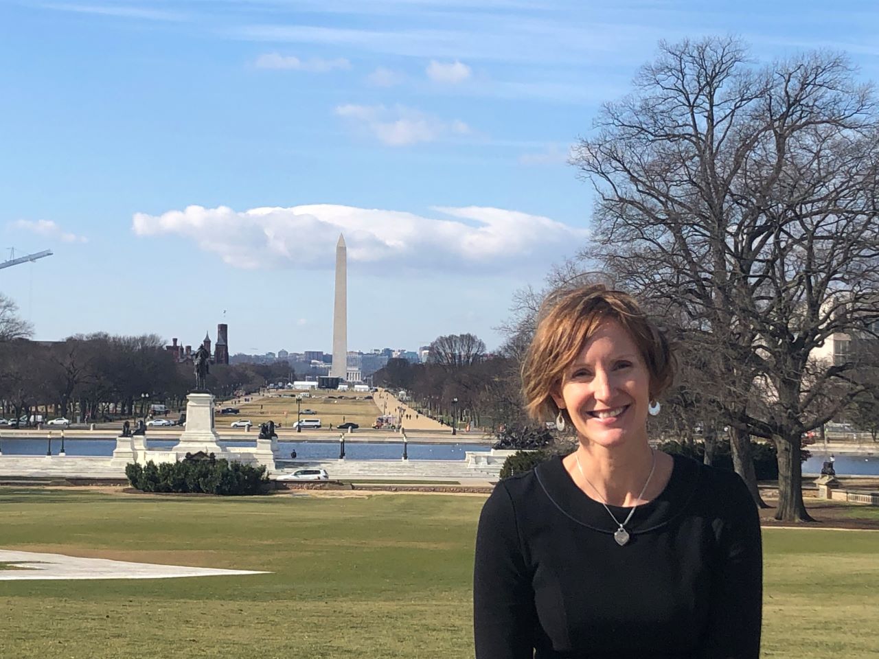 Susan Webb Yackee sits in front the National Mall with the Washington Monument in the distance.