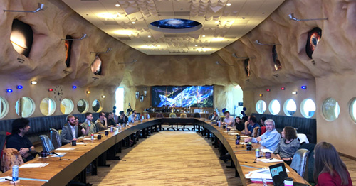 Students, faculty, and staff sit in a outer space themed meeting room