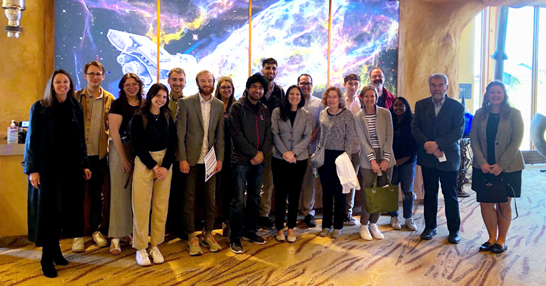 Students, faculty, and staff pose for a group photo in front of artwork depicting outer space.