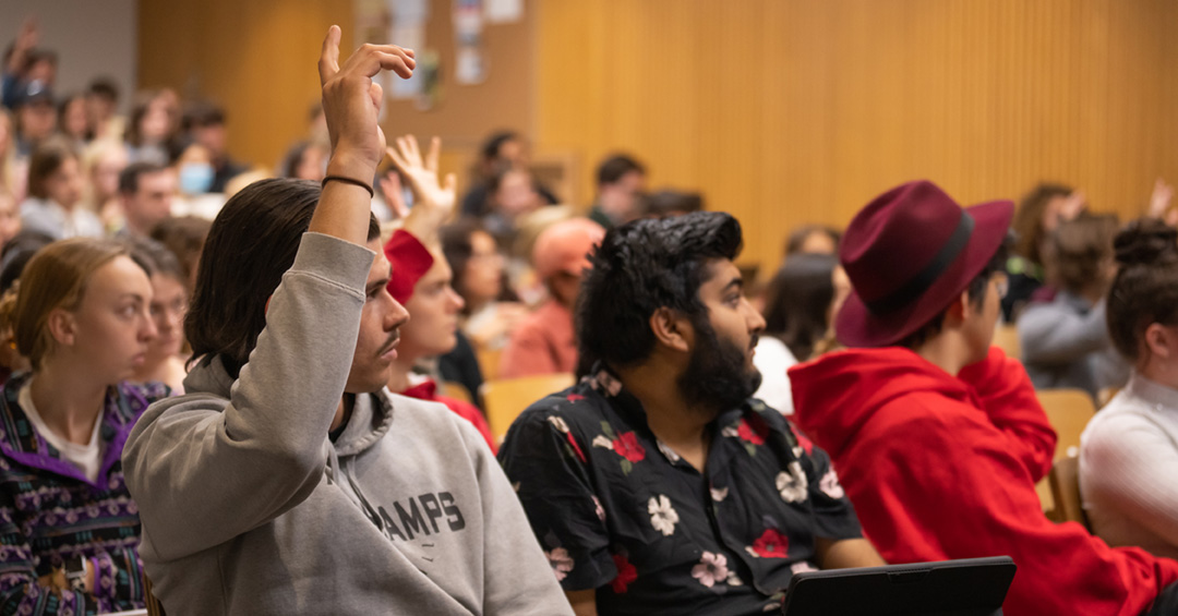 A student raises their hand in a crowded auditorium.