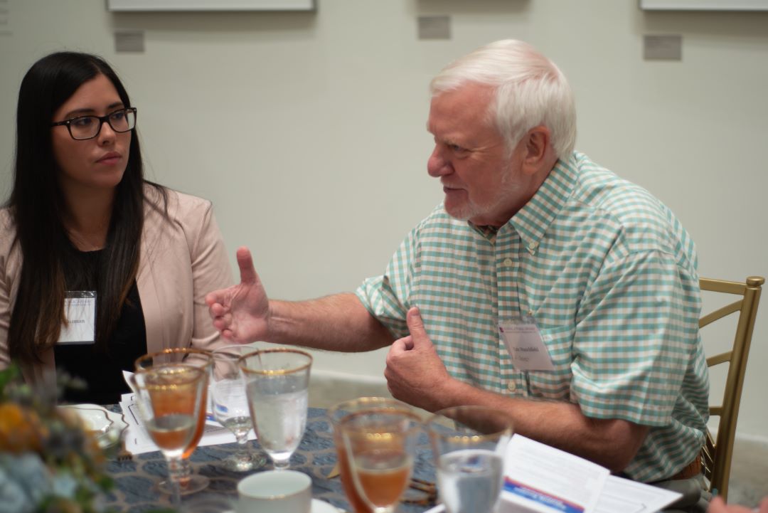 While seated at a table, Eric Stanchfield talks to an attendee