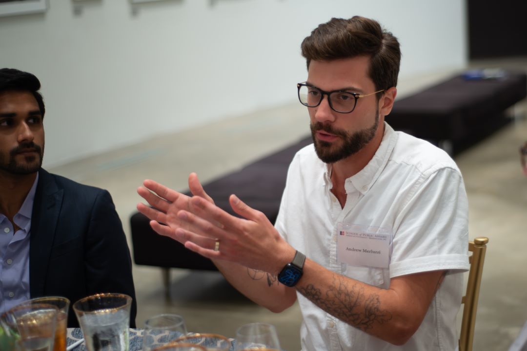 Andrew Merluzzi gestures while talking to other attendees seated nearby.