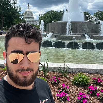 JP Gutierrez takes a selfie with a fountain and the US Capitol in the background