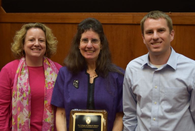 Marjorie Matthews holds an award and stands between Steve Kulig and Hilary Shager.