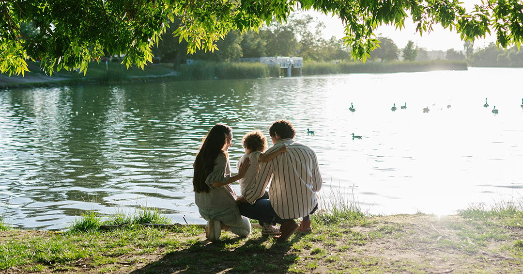 Parents hold their child next to a pond.
