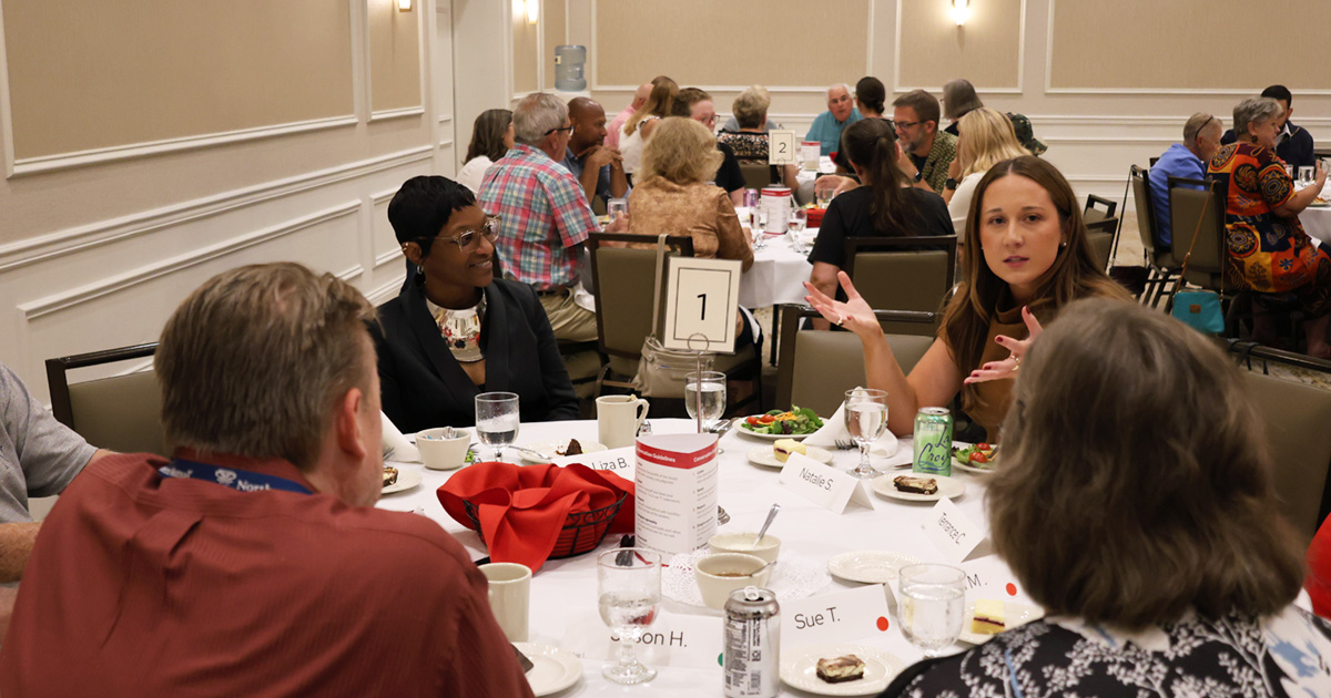 A facilitator speaks to attendees seated around a table in a banquet hall.