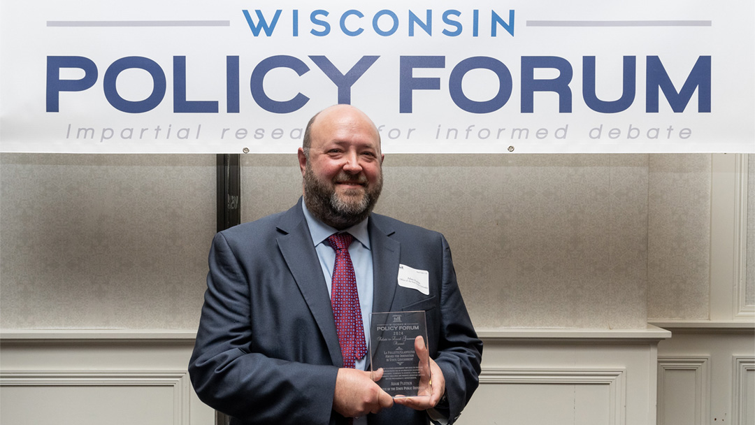 Adam Plotkin holds an award in front of a Wisconsin Policy Forum sign.