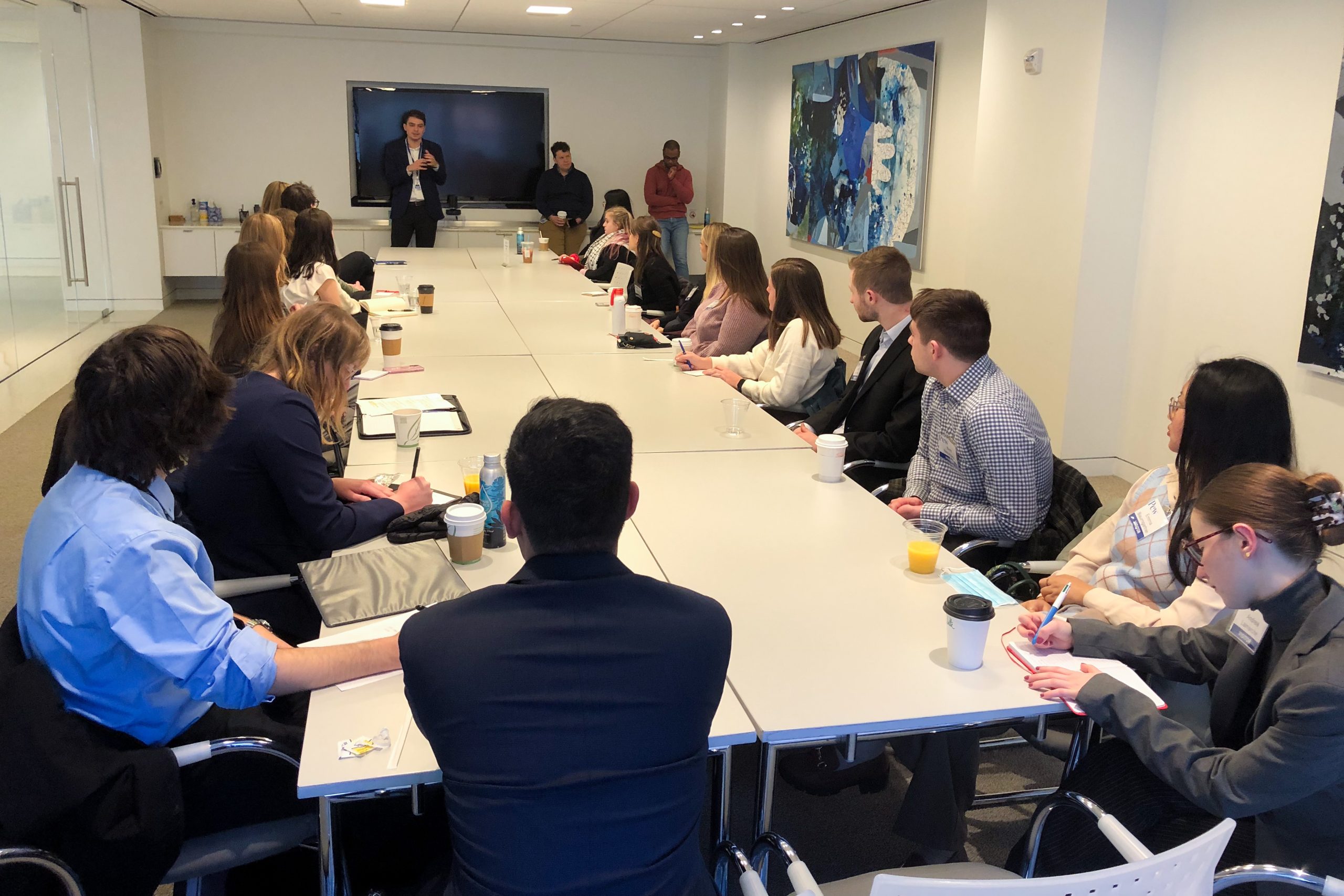 Students sit around a conference room and listen to a speaker