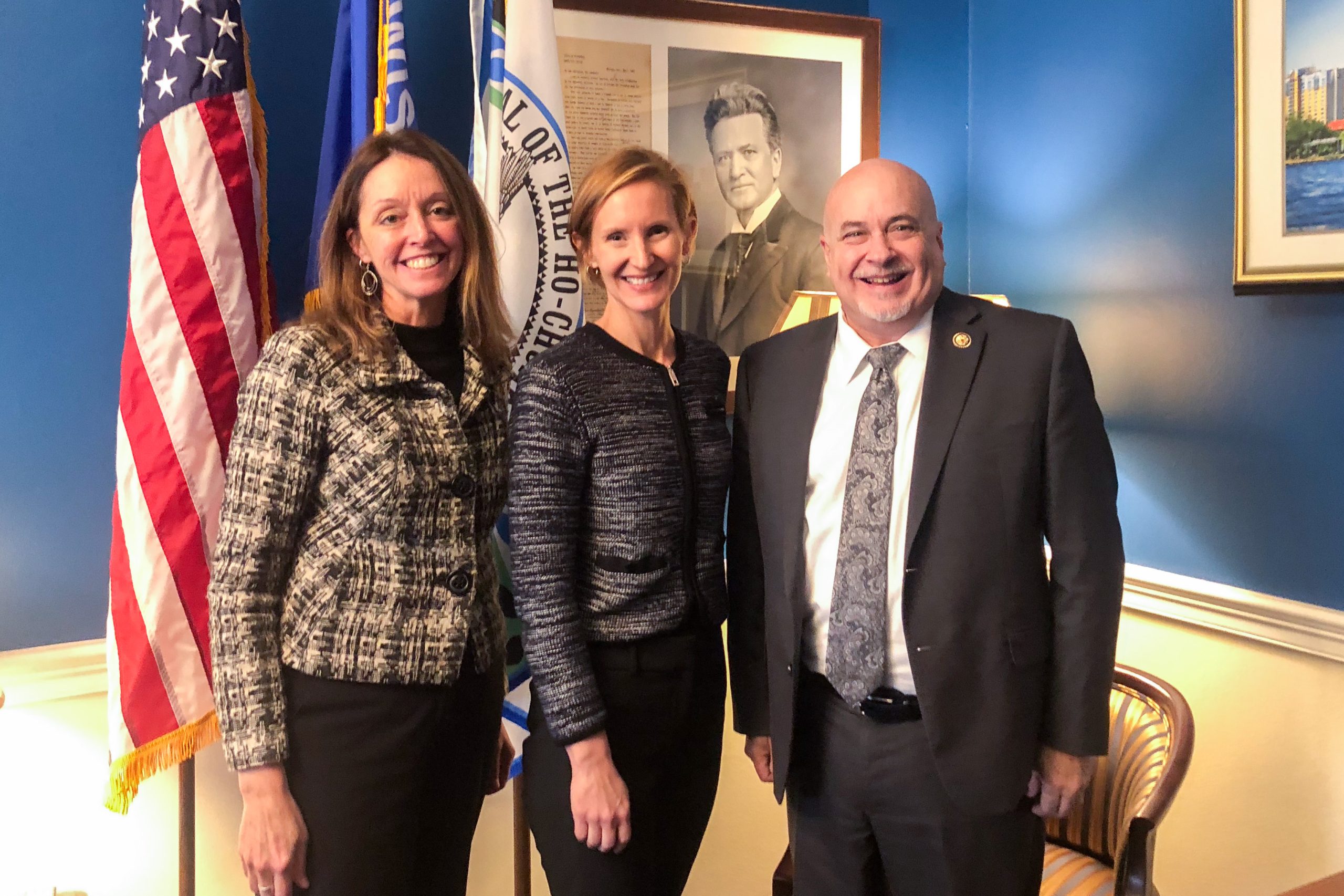 Lisa Ellinger and Susan Yackee pose with Mark Pocan in front of an American flag 