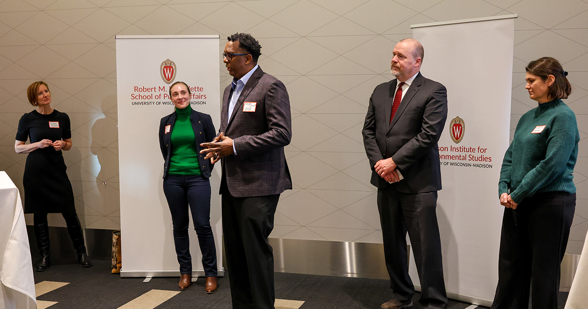 Panelists stand and speak to an audience