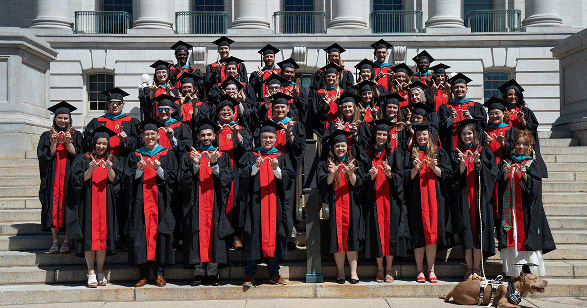 Graduates pose for a photo on the steps of the Wisconsin Capitol building, making the shape of a "W" with their hands
