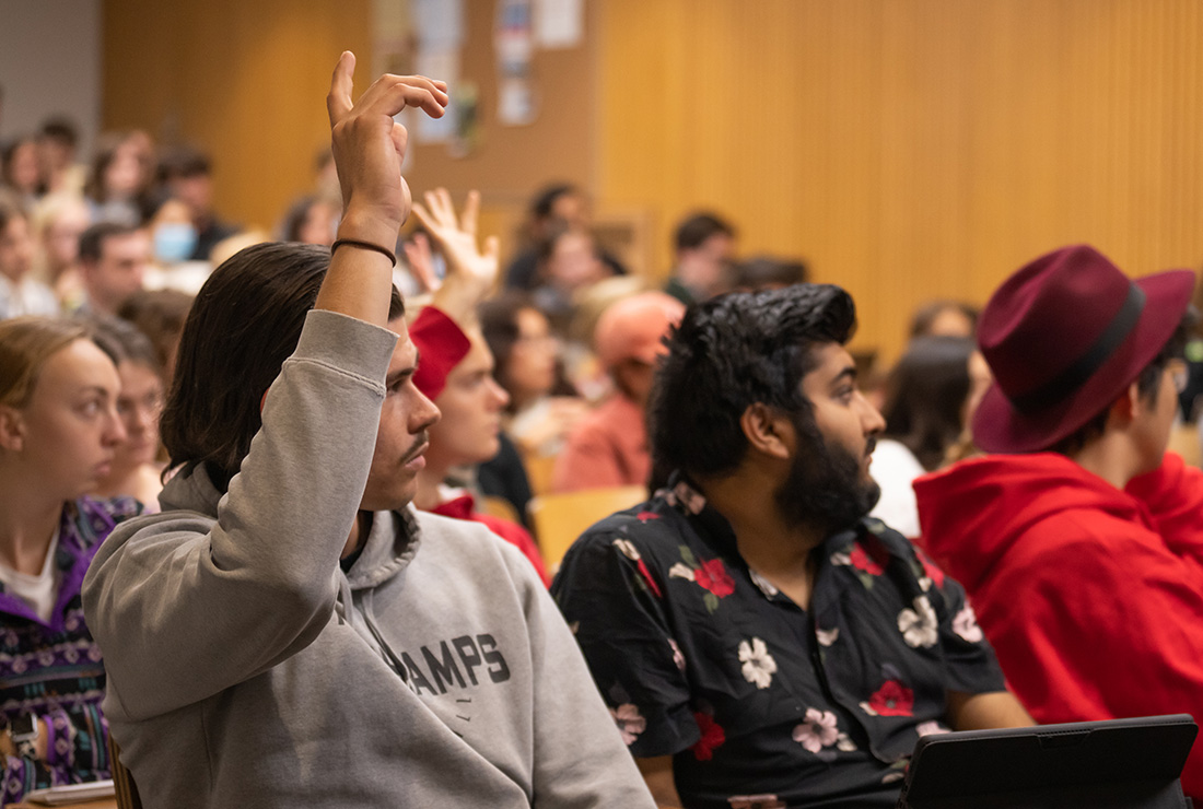 A student raises their hand in a crowded lecture hall.