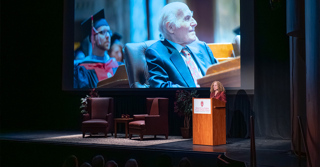 Chancellor Mnookin addresses an audience in Shannon Hall with a photo of Senator Herb Kohl displayed on a projector screen.