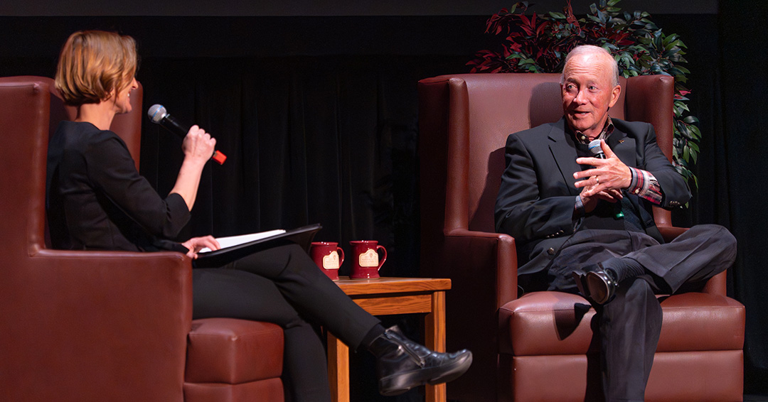 Mitch Daniels addresses Susan Yackee while seated on a stage.