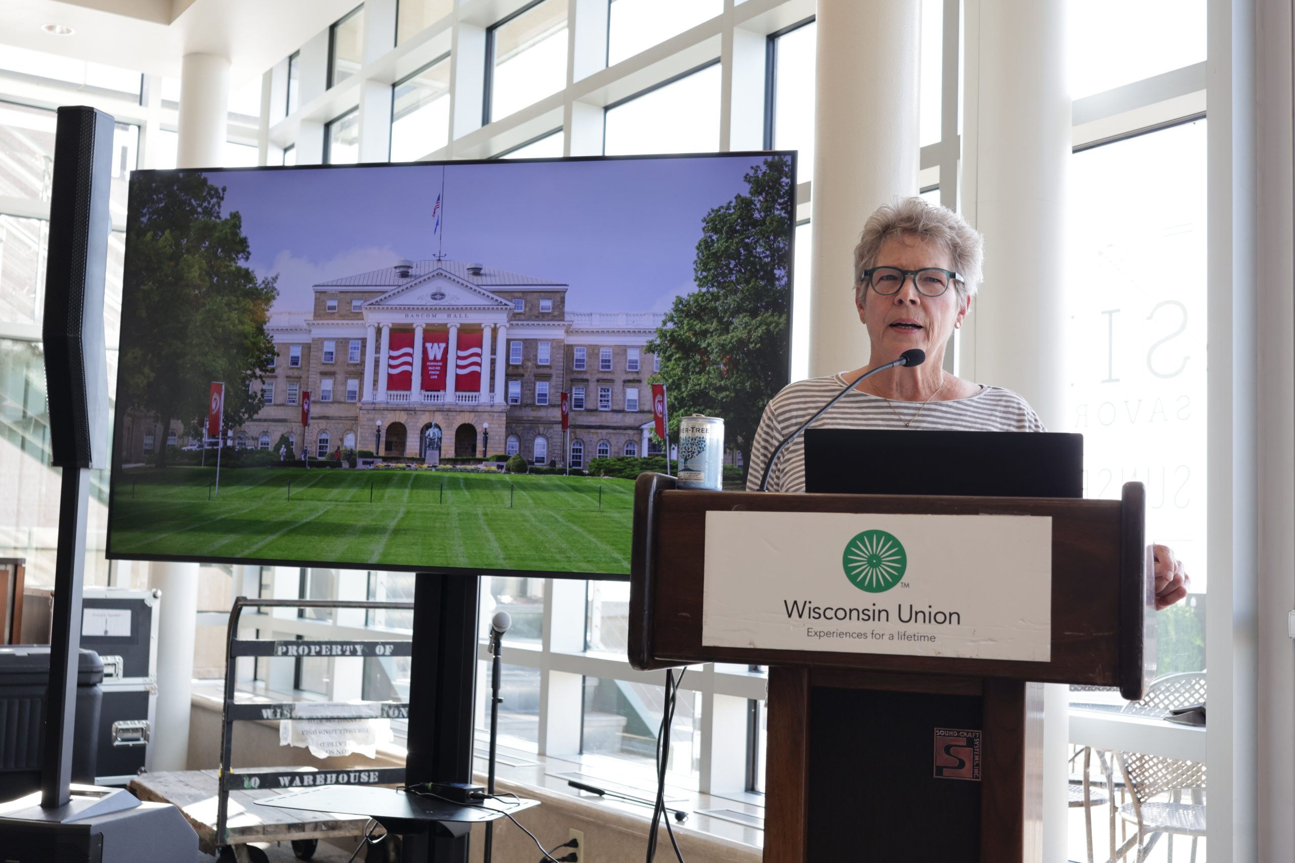 A woman stands at a podium with a screen behind her that shows Bascom Hall