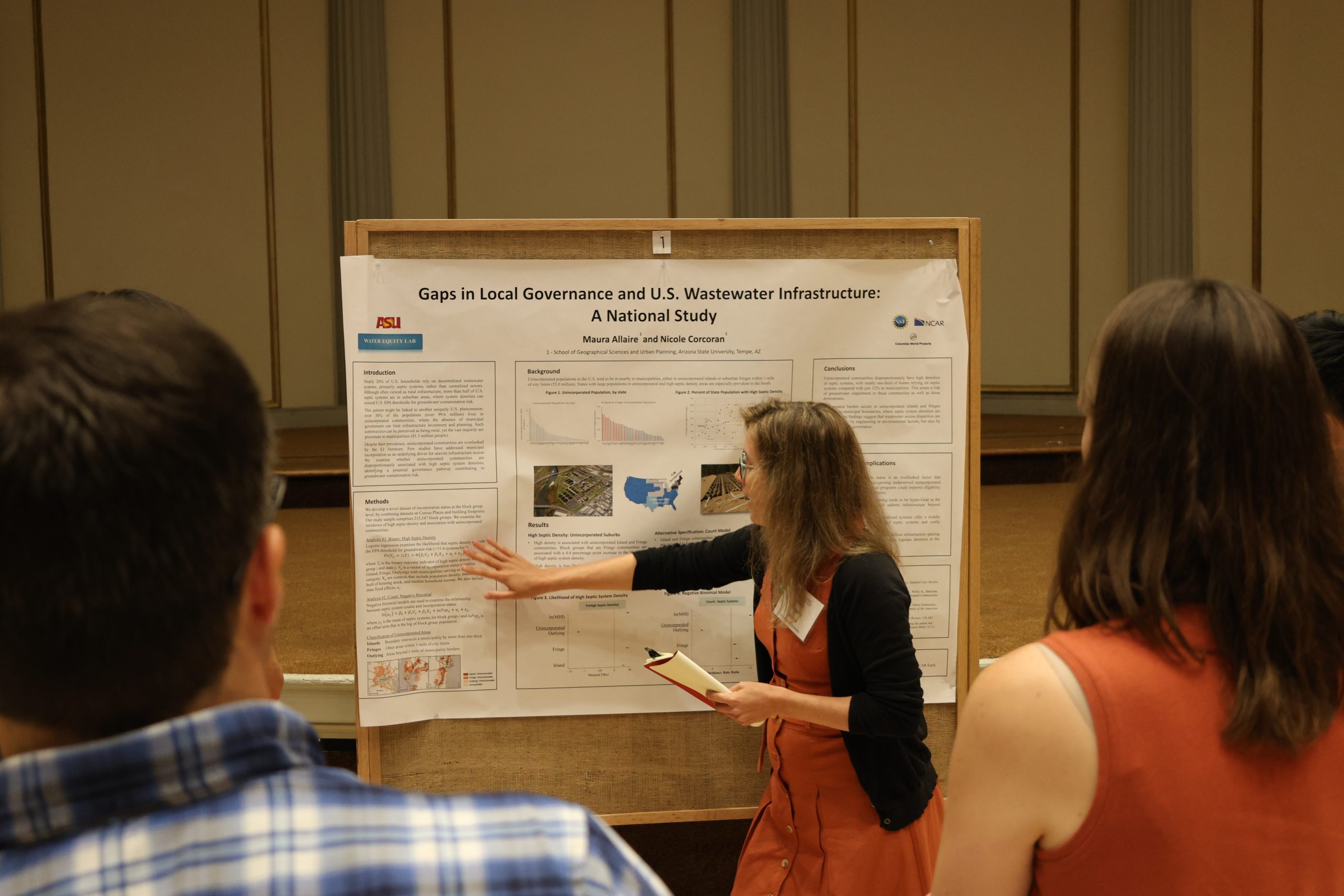 A woman stands in front of an academic poster, pointing to text and figures