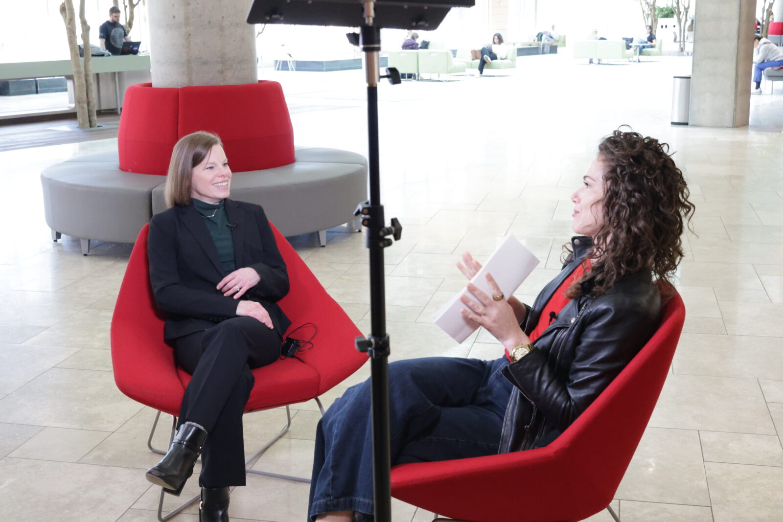 Amber Wichowsky smiles while sitting in a red chair on the left and Kristin Brey sits in a red chair on the right.